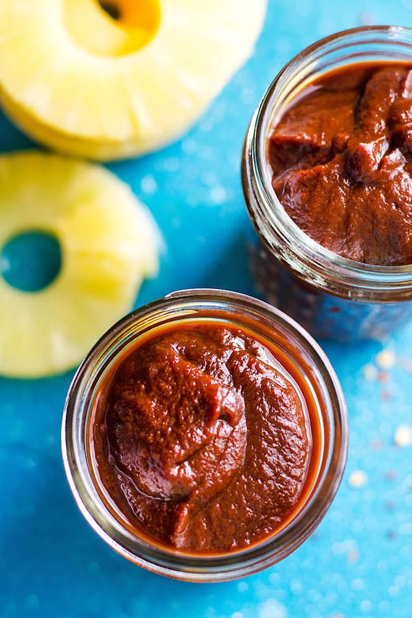 Hawaiian BBQ Sauce in glass jars with pineapple slices on a counter.