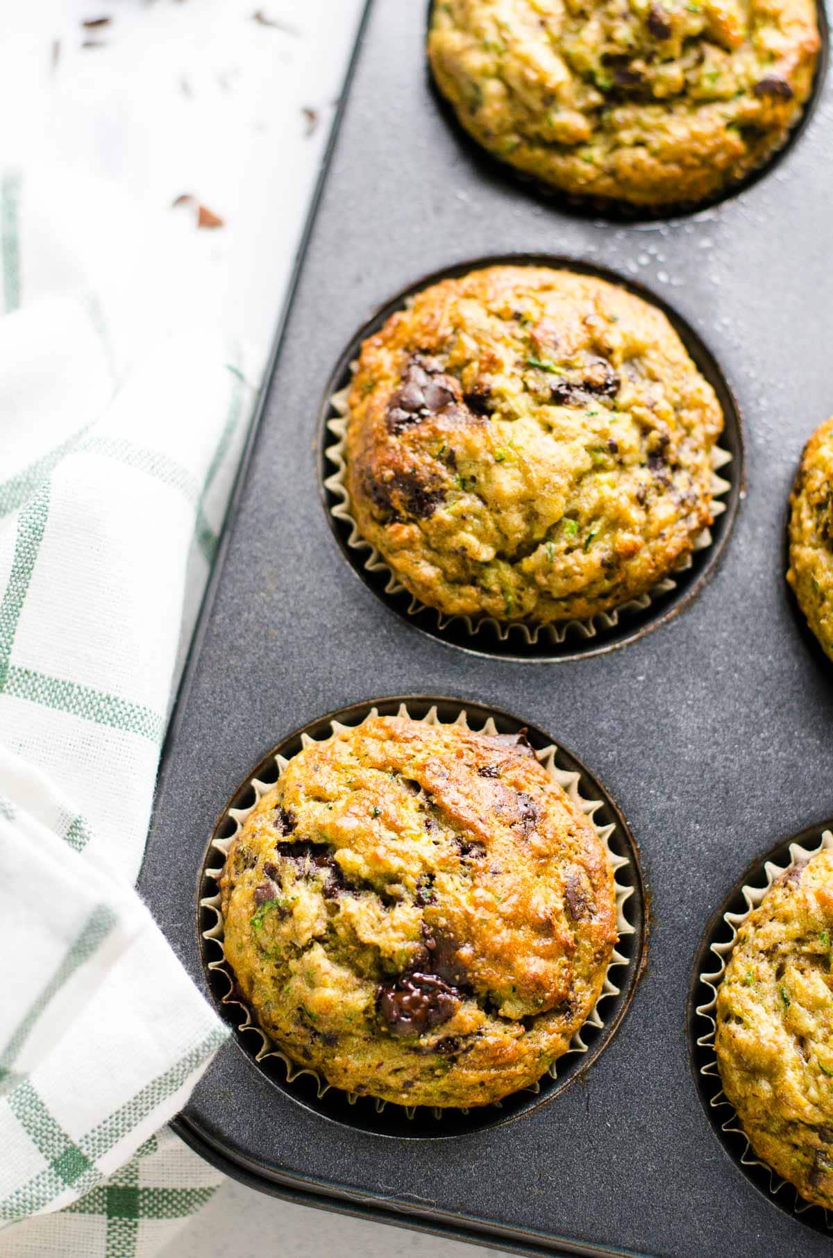 Healthy banana zucchini muffins in a muffin tin with a towel.
