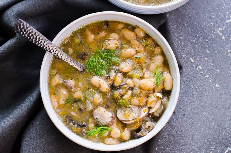 Bowl of mushroom bean soup garnished with dill.