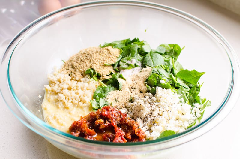 glass bowl with cooked quinoa, spinach, feta, sun dried tomatoes, eggs, spices