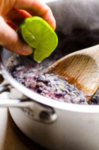 squeezing lime into pot of black beans with wooden spoon
