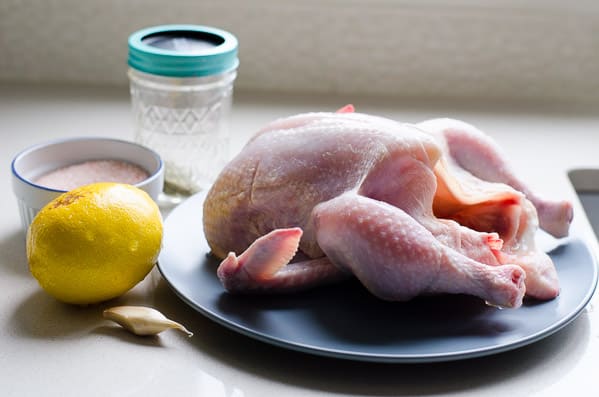 Whole chicken, lemon, garlic, salt and spices on the kitchen counter.