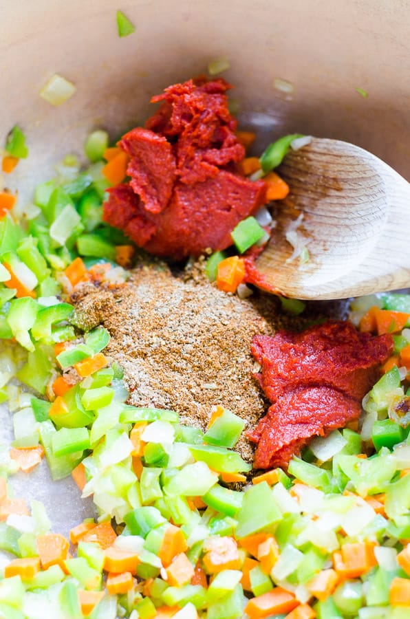 celery, carrots, tomato paste and spices in blue pot with wooden spoon
