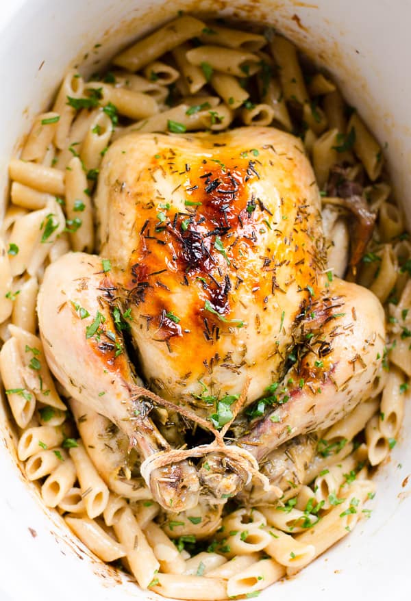 Roasted whole chicken on top of cooked pasta garnished with parsley in slow cooker.