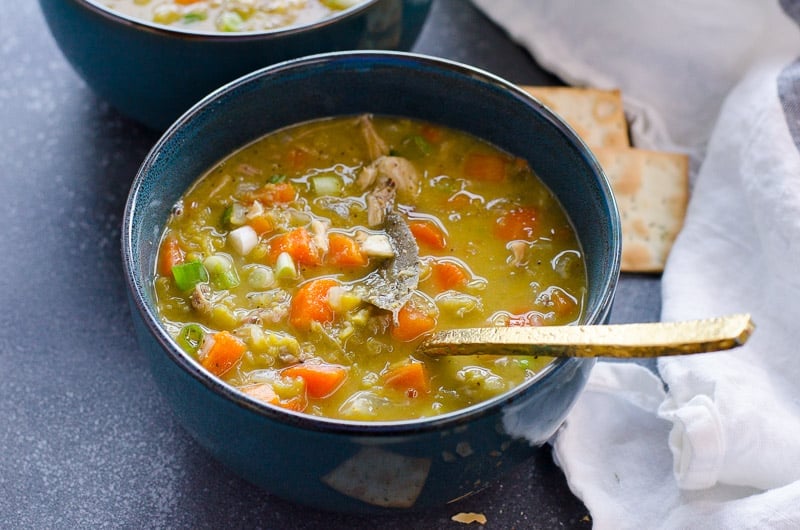 Bowl of green split pea soup with crackers and spoon.