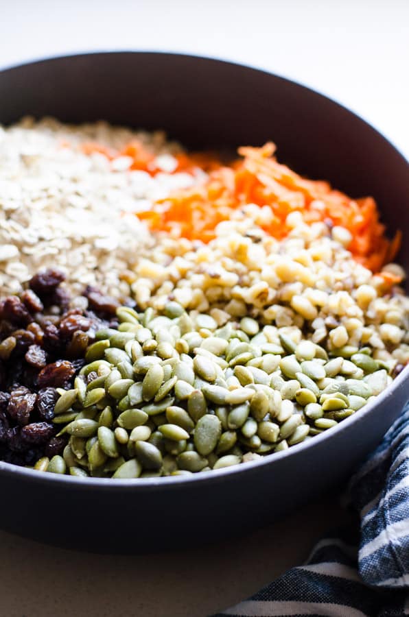 Grated carrots, oats, chia seeds, raisins, walnuts, pumpkin seeds in a grey bowl.