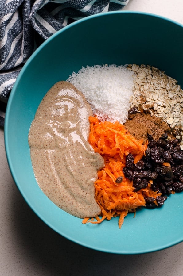 Oats, shredded carrots, nut butter, coconut and raisins in blue bowl.