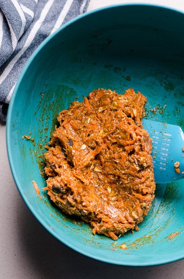 Carrots, nut butter, oats, raisins mixed together in blue bowl.