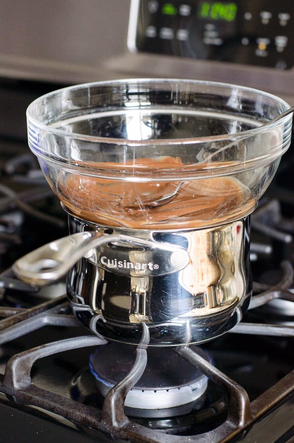 Melting chocolate in glass bowl over pot with water on stove.