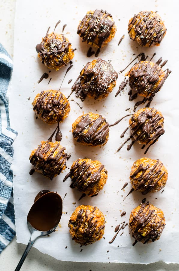 Carrot cake truffles drizzled with chocolate on parchment paper.