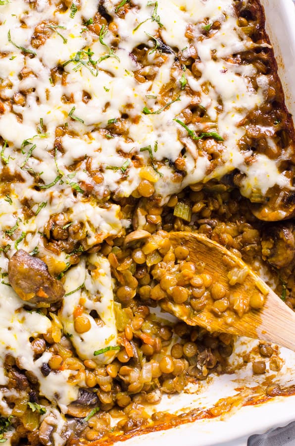 Lentil casserole with mushrooms and melted cheese on top and wooden spoon in a baking dish.
