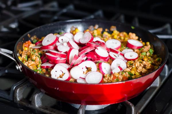 Radishes added to red skillet on stove.