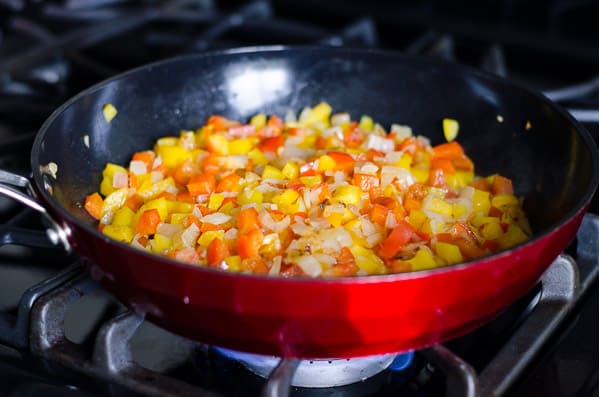 Onion and bell peppers in red skillet on stove. 