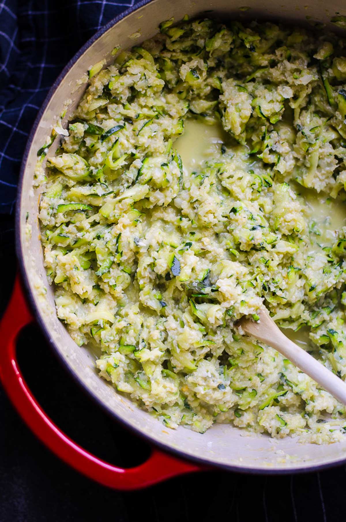 Cheesy cauliflower rice with zucchini in a red dutch oven with spoon.