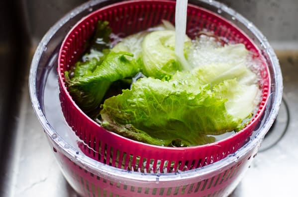 washing lettuce under running water in salad spinner