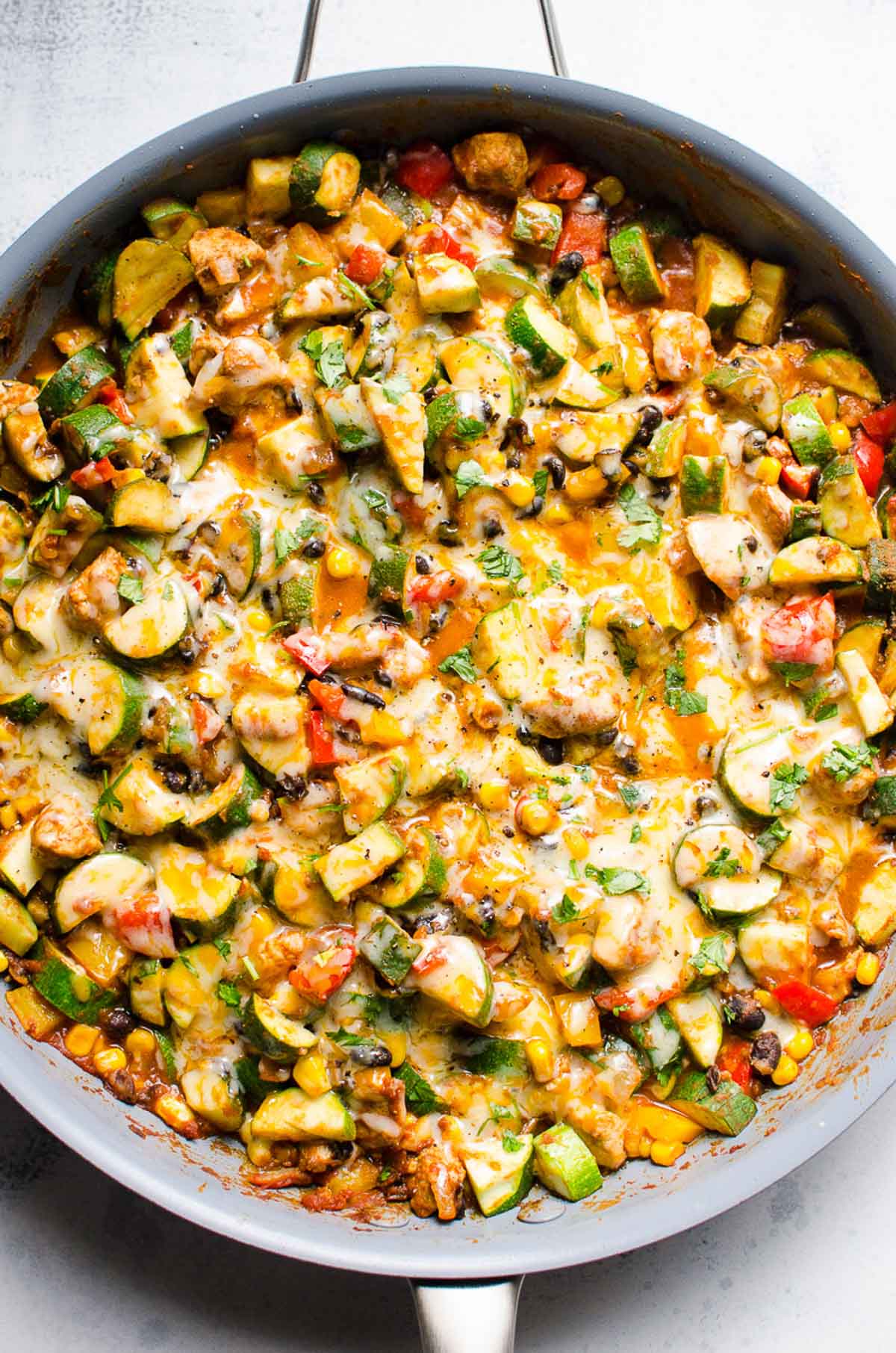 Tex Mex chicken and zucchini with melted cheese and cilantro in blue skillet.