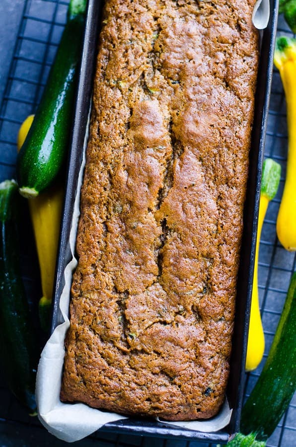 Healthy zucchini bread in a loaf pan with fresh zucchini by the sides.