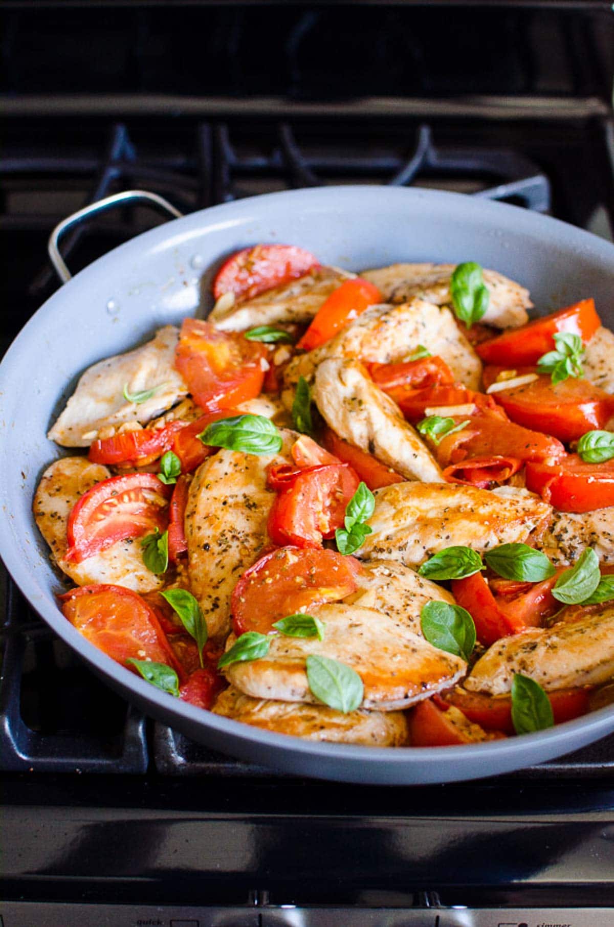 Chicken with tomatoes and garlic garnished with basil in a skillet.