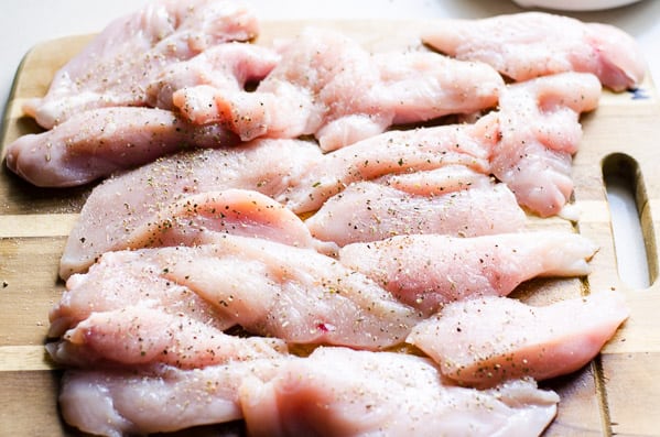 Chicken on a cutting board sprinkled with salt and pepper.