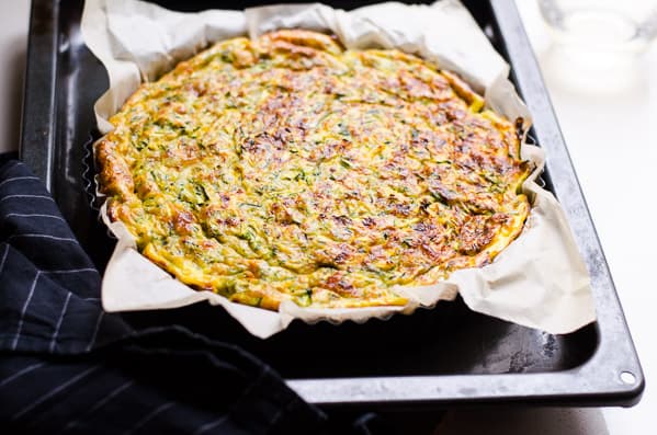 Zucchini quiche finished baking in a baking pan with a towel nearby.