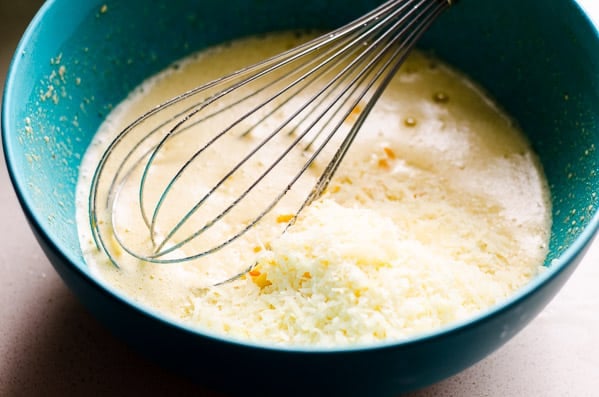 Cheese and egg and flour mixture in blue bowl with a whisk.