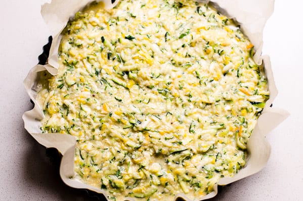 Unbaked zucchini quiche in a tart pan lined with parchment paper.