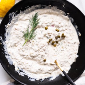 Greek yogurt tartar sauce with capers and fresh dill in a black bowl with fork.