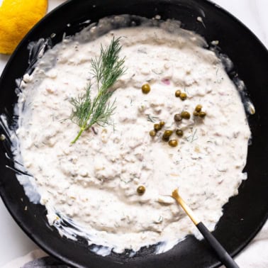 Greek yogurt tartar sauce with capers and fresh dill in a black bowl with fork.