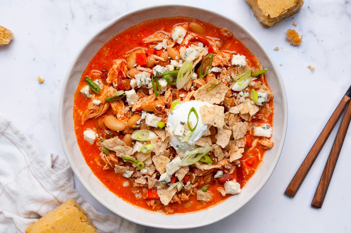 Buffalo chicken chili with crushed corn tortilla chips, sour cream, blue cheese, and green onion in a bowl.