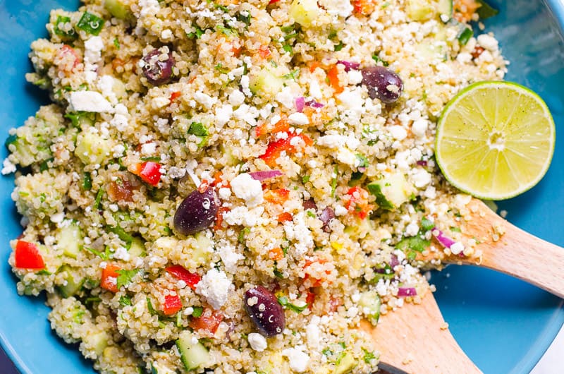 mediterranean quinoa salad served in a blue bowl with a slice of lime and wooden serving spoons