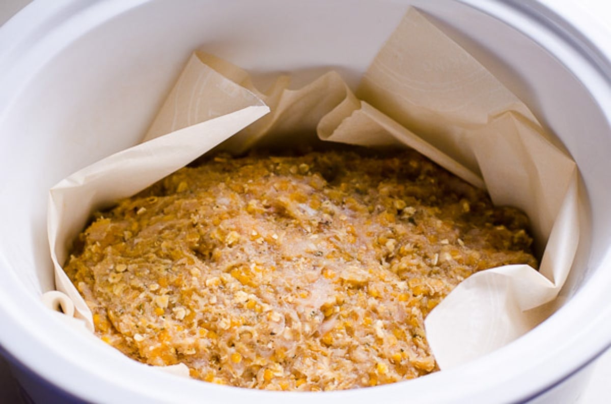 Uncooked turkey meatloaf in a slow cooker lined with parchment paper.