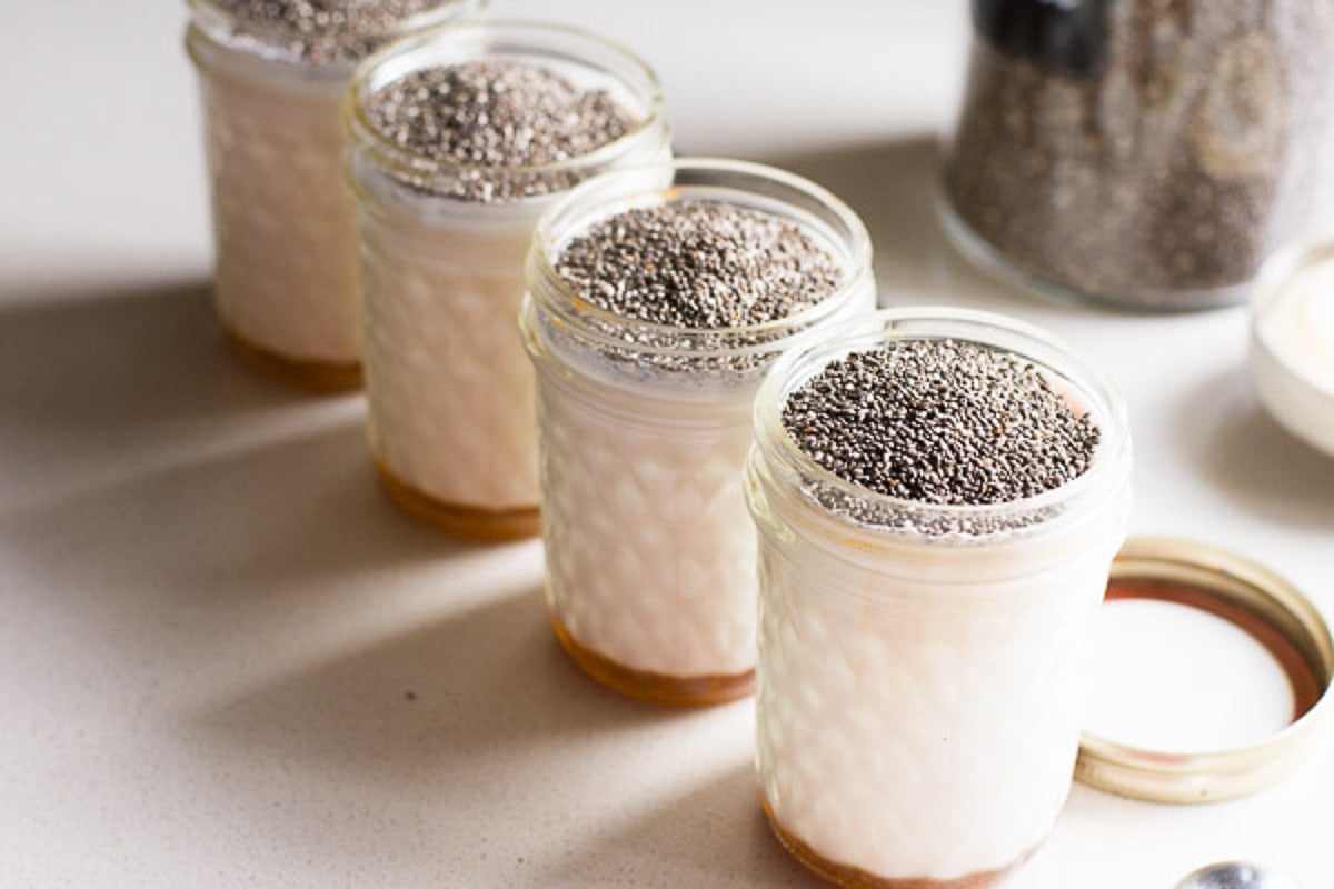 Chia seeds added on top of almond milk, maple syrup and vanilla extract in glass jars.