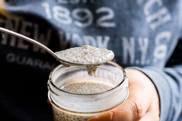 A spoon with chia seed pudding being held over a jar of chia pudding.