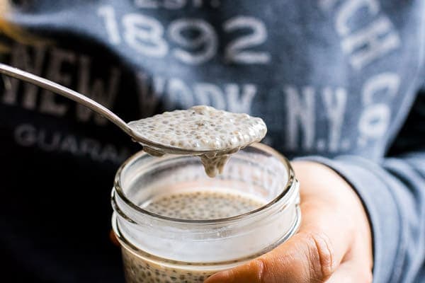 Person holding a spoon with vanilla chia seed pudding over a jar of chia pudding.