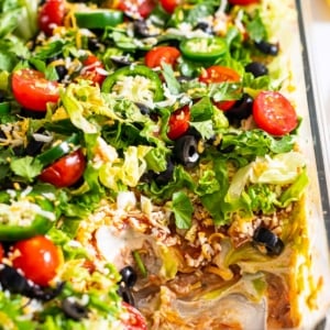 Healthy seven layer dip garnished with jalapenos and olives and served in a baking dish showing texture inside.