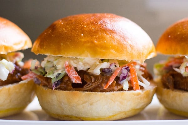 Healthy pulled pork sandwich with coleslaw on white serving dish.