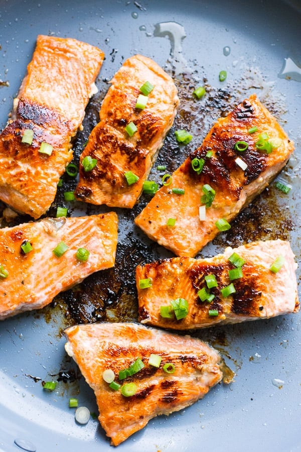 Honey garlic salmon in skillet with green onion garnish.