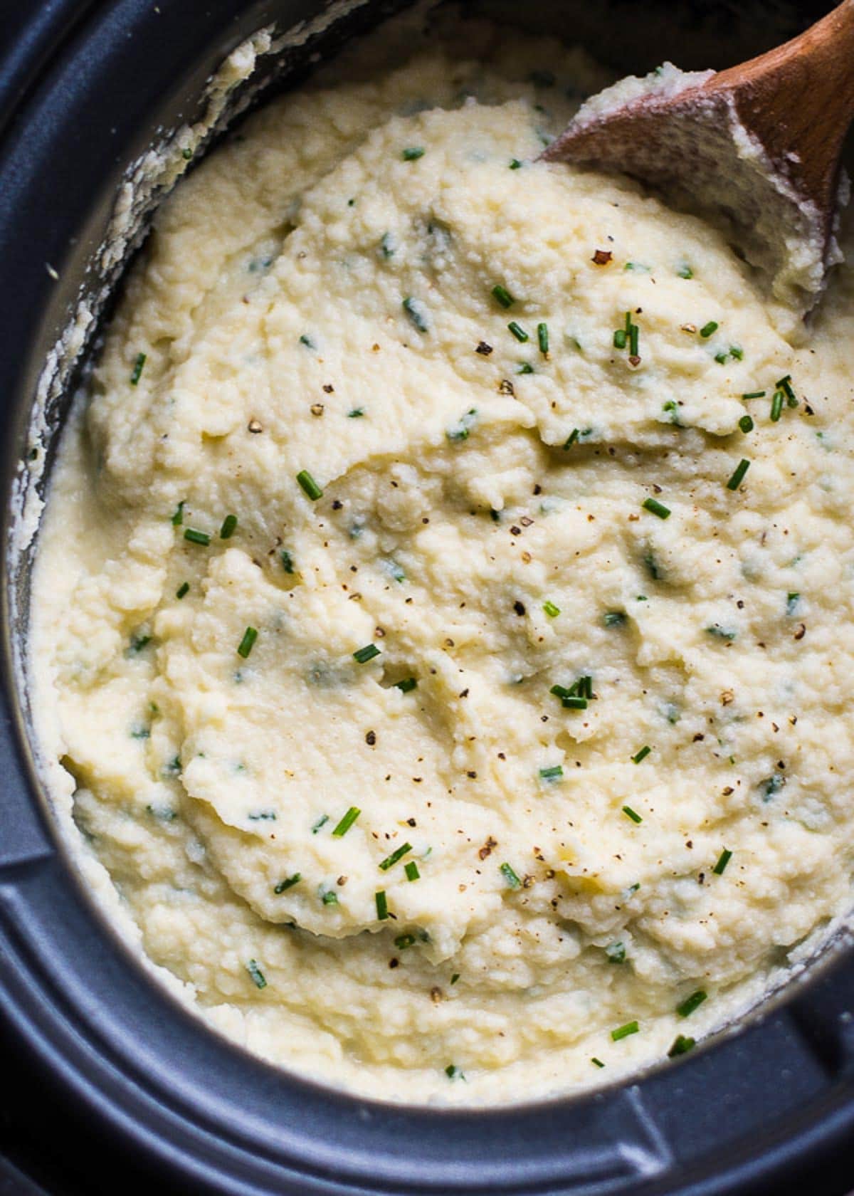 Slow cooker cauliflower mashed potatoes garnished with chives and a serving spoon.