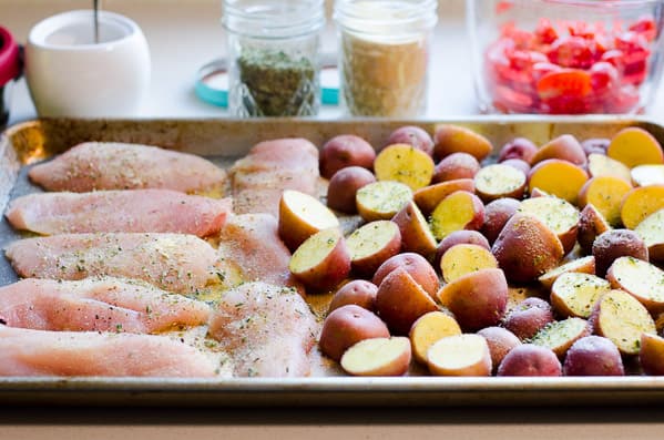 Raw chicken and potatoes on baking sheet.