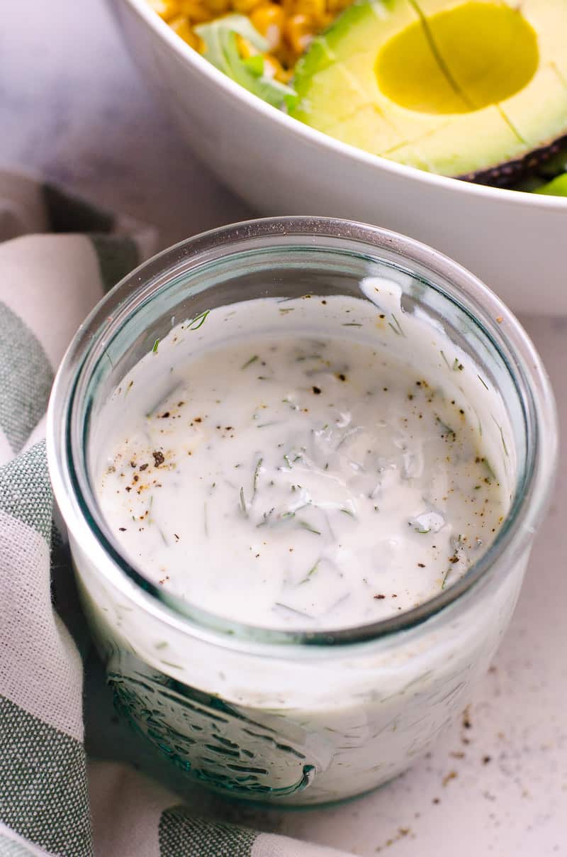 Healthy Ranch Dressing in a glass jar next to a salad bowl