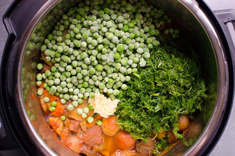 Peas, dill and fresh garlic with cooked beef stew in Instant Pot.