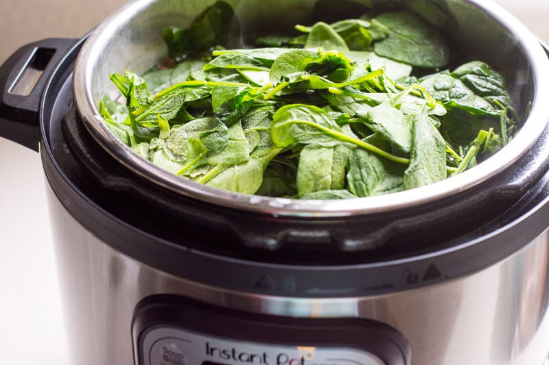 Adding fresh spinach to the pot.