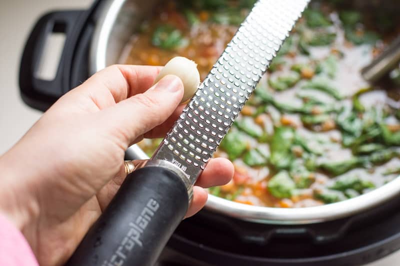 Grating fresh garlic into soup with grater.