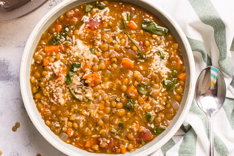 Instant Pot lentil soup garnished with Parmesan cheese in a bowl. Spoon and towel on a counter.