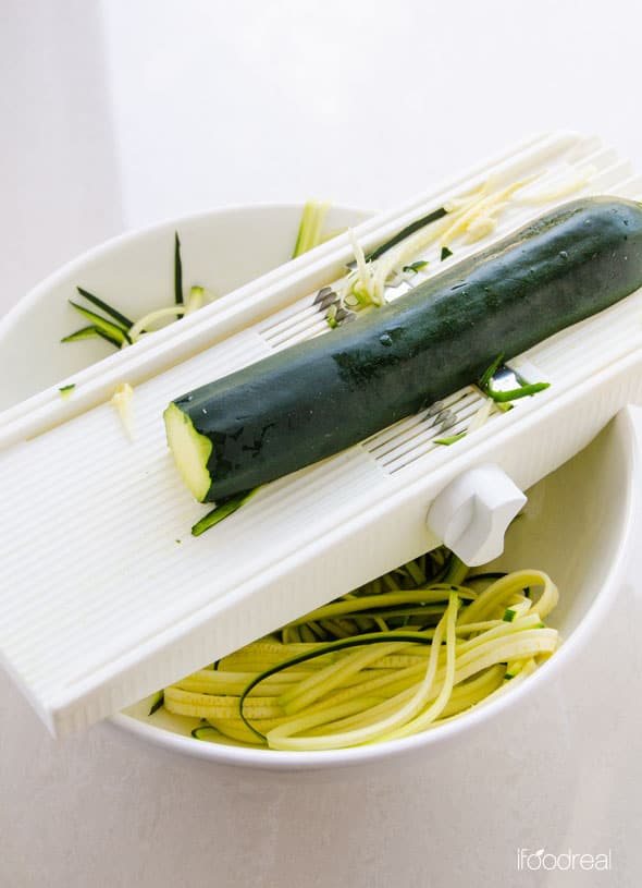 Zucchini on top of mandoline being sliced into zoodles over a bowl.