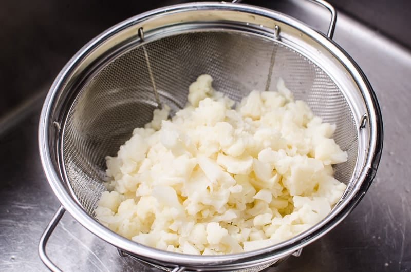 cauliflower being drained for cauliflower mashed potatoes