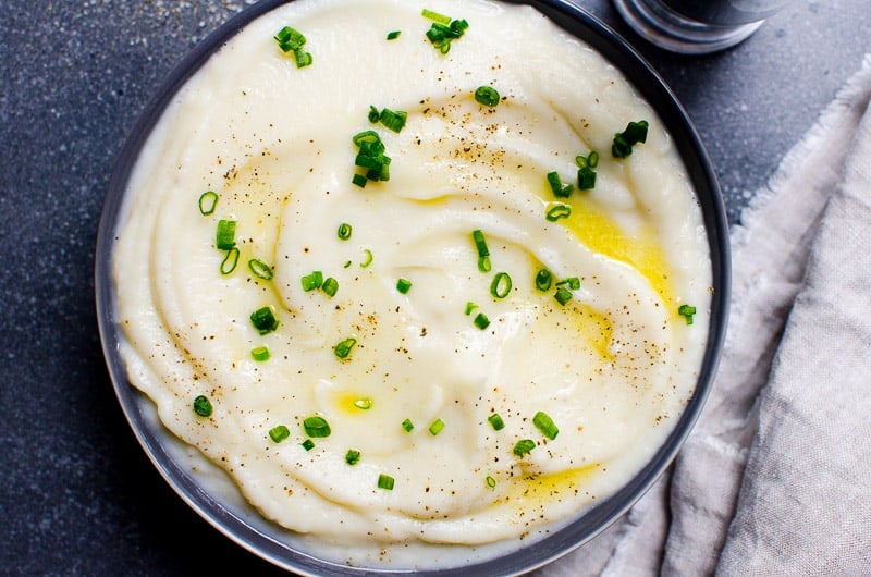 Mashed cauliflower in a bowl, linen and pepper mill on a countertop nearby.