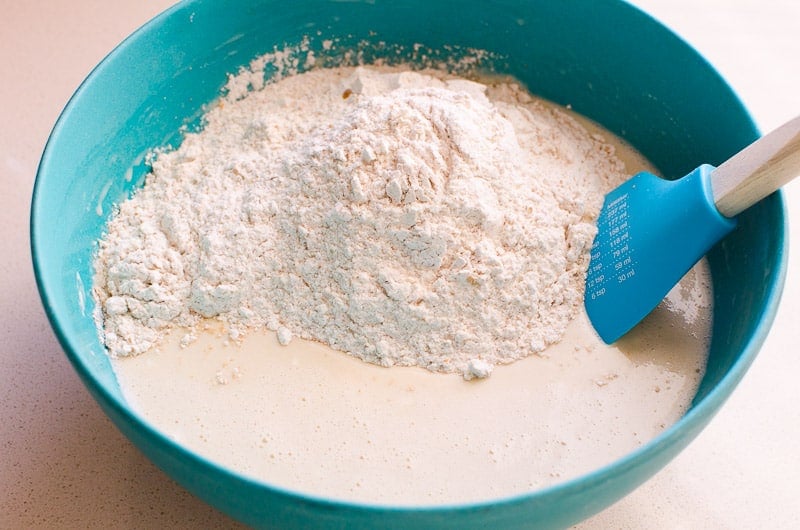 Whole wheat flour with wet ingredients in blue bowl with spatula.