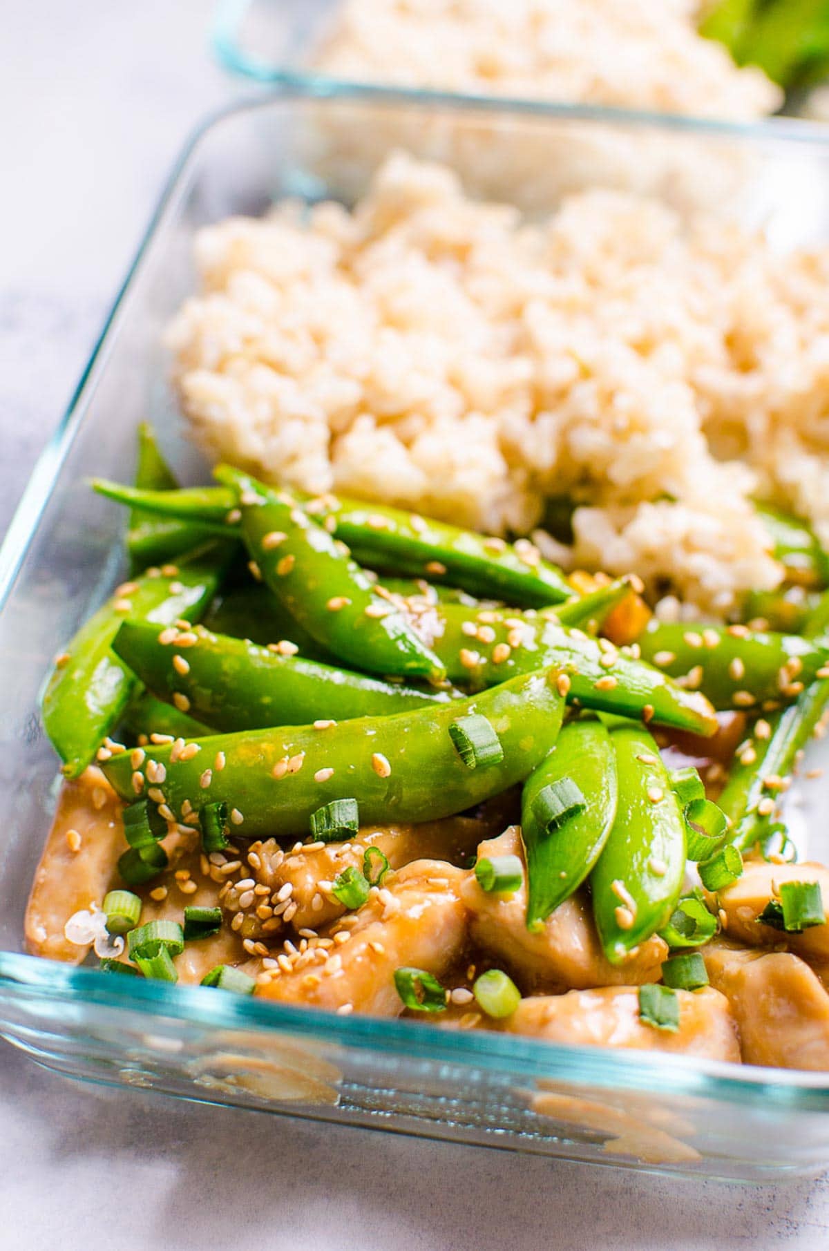 Closeup of glass container with chicken, snap peas and brown rice. 