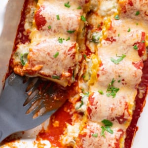 Chicken lasagna roll ups in a baking dish with one missing and spatula in it.